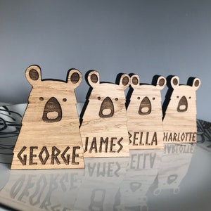 May include: Four wooden bear place card holders with the names George, James, Bella, and Charlotte engraved on them.