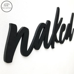 May include: Black wooden sign with the word "naked" written in a cursive font.