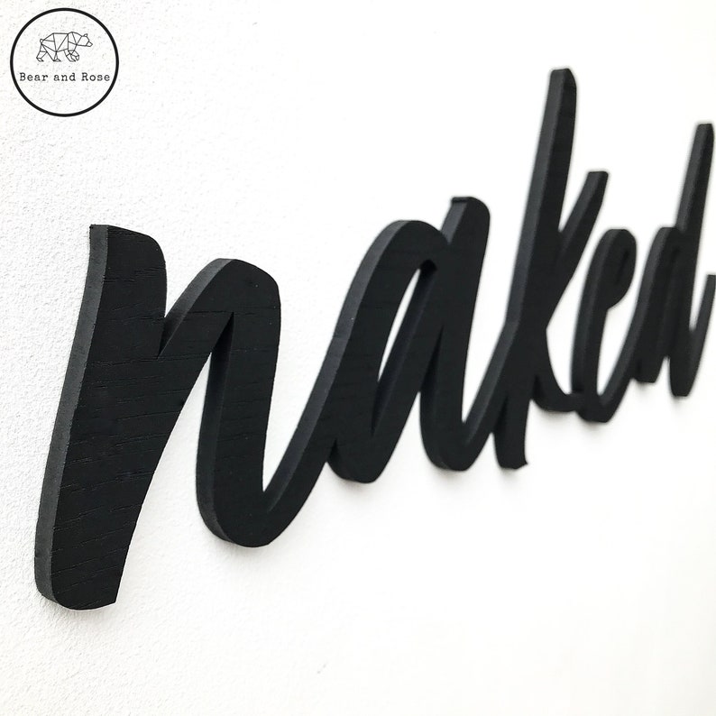 May include: Black wooden sign with the word "naked" written in a cursive font.