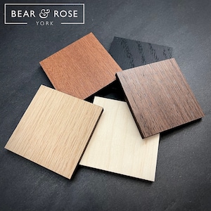 May include: Five wood veneer samples in different colours and grain patterns. The samples are arranged in a pile on a black surface. The samples are labelled "BEAR & ROSE YORK".