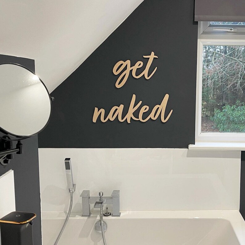 May include: A bathroom with a white bathtub and a black wall with the words "get naked" written in cursive on it.
