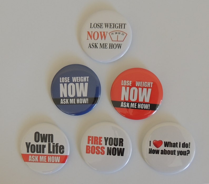 May include: Six round button badges with motivational slogans. The badges are white, red, blue, and black with white text. The slogans include "Lose Weight Now Ask Me How", "Own Your Life Ask Me How", "Fire Your Boss Now", and "I What I Do! How About You?"