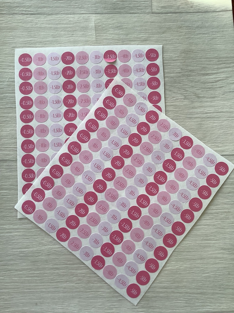 May include: Two sheets of pink and light pink circular stickers with black text indicating weight loss in pounds. The stickers range from -0.5lb to -5lb. The stickers are arranged in rows and columns.