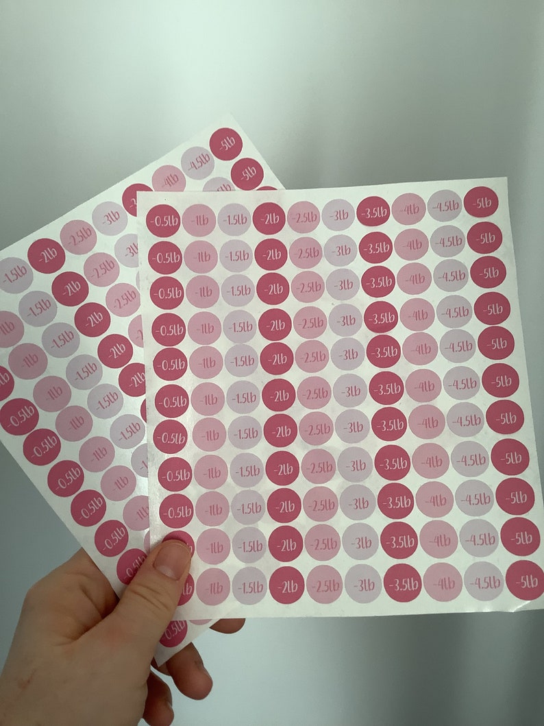 May include: Two sheets of pink and light pink round stickers with weight loss measurements in pounds. Each sticker has a number from -0.23kg to -2.27kg. The stickers are on a white background.