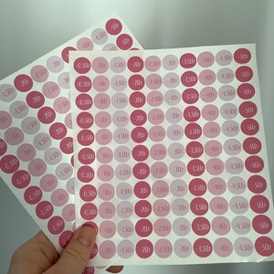 May include: Two sheets of pink and light pink round stickers with weight loss measurements in pounds. Each sticker has a number from -0.23kg to -2.27kg. The stickers are on a white background.