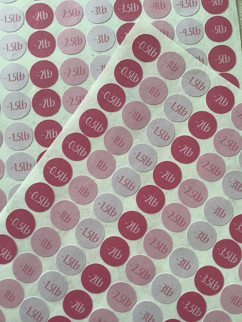 May include: Circular stickers in varying shades of pink and red, each printed with a weight measurement in pounds. The stickers range from -0.5lb to -5lb. The stickers are arranged on a light-colored sheet.