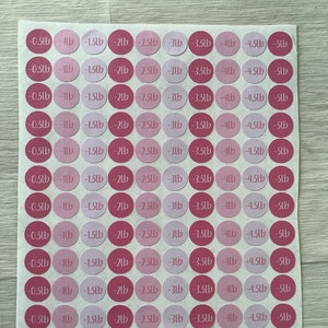 May include: A sheet of pink and light pink circular stickers. Each sticker has a weight measurement in pounds, ranging from -0.5lb to -5lb. The stickers are arranged in a grid pattern on a white background.