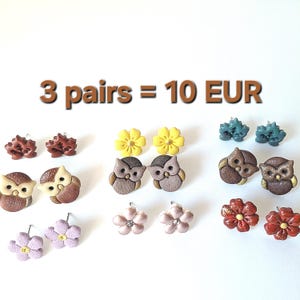 Op de afbeelding: Een verzameling kleurrijke oorstekers in diverse ontwerpen, waaronder uilen, bloemen en stekelige vormen. De oorbellen zijn gerangschikt op een witte ondergrond. De tekst "3 pairs = 10 EUR" staat boven de oorbellen.