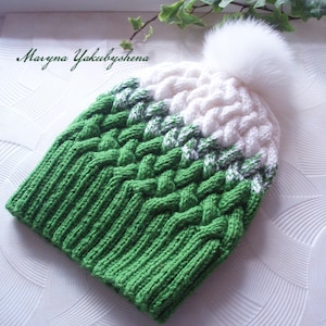 May include: A knitted winter hat in green and white with a large white pom-pom. The hat features a textured, braided design and the name "Maryna Yakubyshena" in script.