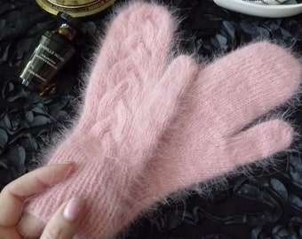 Può includere: Un paio di guanti di lana rosa e pelosi con un motivo a treccia. I guanti sono morbidi e soffici, e sarebbero perfetti per tenere le mani al caldo in inverno.