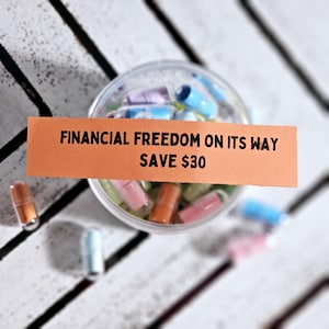 May include: Orange and white paper strip with the text "FINANCIAL FREEDOM ON ITS WAY SAVE &pound;30". A clear plastic container filled with colourful capsules.