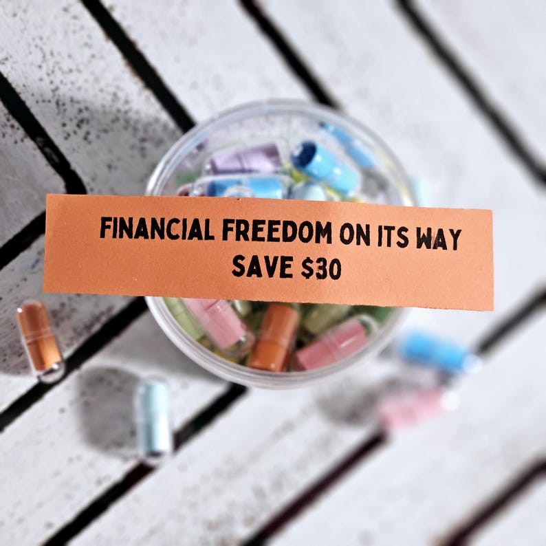 May include: Orange and white paper strip with the text "FINANCIAL FREEDOM ON ITS WAY SAVE &pound;30". A clear plastic container filled with colourful capsules.