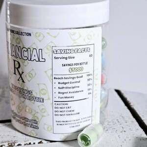 May include: A white plastic jar with a green and white label that reads "Saving Facts" and "&pound;5000". The label also includes a list of savings goals and percentages. The jar is filled with small, colourful pills.
