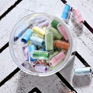 May include: A clear plastic jar filled with colourful capsules containing rolled up paper notes. The capsules are in various shades of blue, green, yellow, pink, and purple.