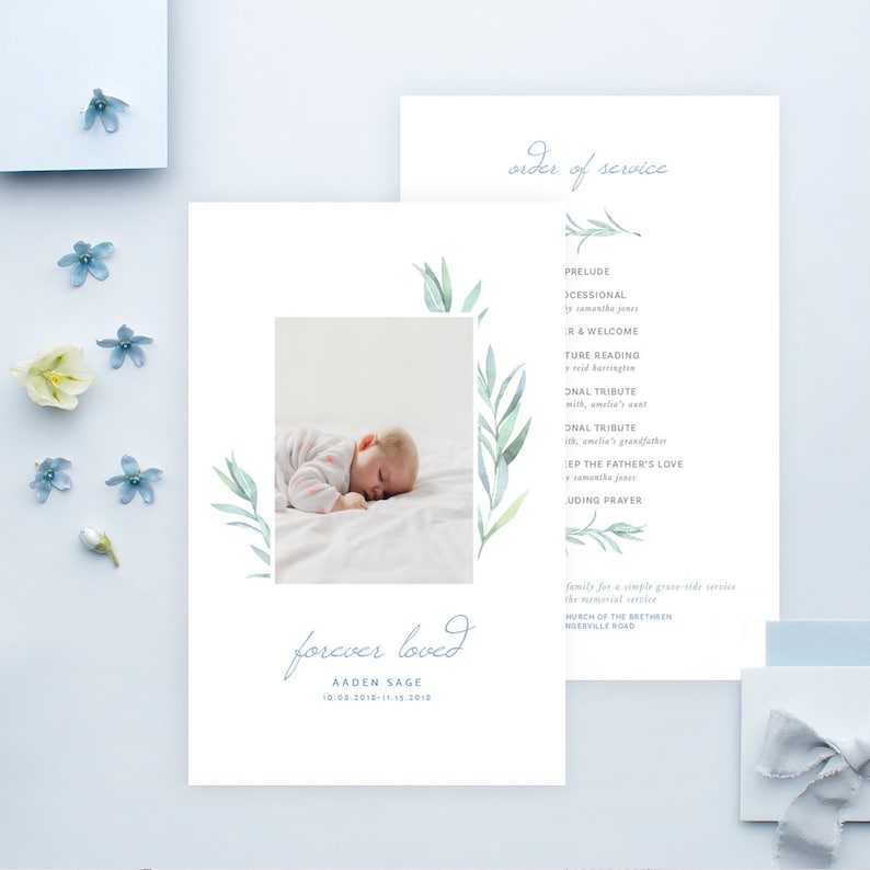 Op de afbeelding: Een lichtblauwe en witte kaart met een aquarel-illustratie van bladeren. De kaart toont een foto van een slapende baby en de tekst "forever loved" met de naam "Aaden Sage" en de data "10.08.2010-11.15.2010".