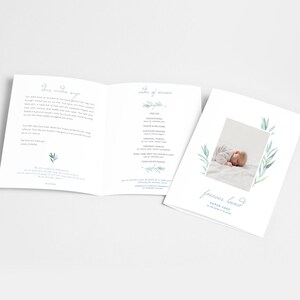 Op de afbeelding: Een wit en blauw begrafenisprogramma met een foto van een slapende baby op een wit deken. Het programma bevat de volgorde van de dienst, een persoonlijk bericht en de woorden "voor altijd geliefd" met de naam en data van de baby.