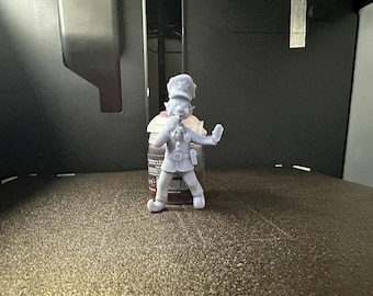 May include: A small, light gray figurine of a character in a police uniform, with a hat and a tie. The figurine is standing on a textured surface, with a bottle of paint in the background.