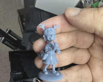 May include: A light blue figurine of a cartoon girl holding a musical instrument and a bag. The figurine is standing on a round base. The girl has two pigtails and is wearing a dress and shoes.