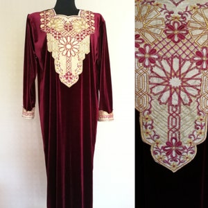 May include: A long, burgundy velvet dress with gold embroidery around the neckline and cuffs. The embroidery features a geometric pattern with floral accents.