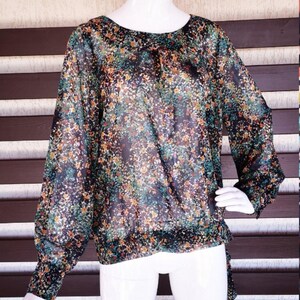 May include: A sheer, long-sleeved blouse with a floral print in shades of black, green, and orange. The blouse has a loose fit and a round neckline.