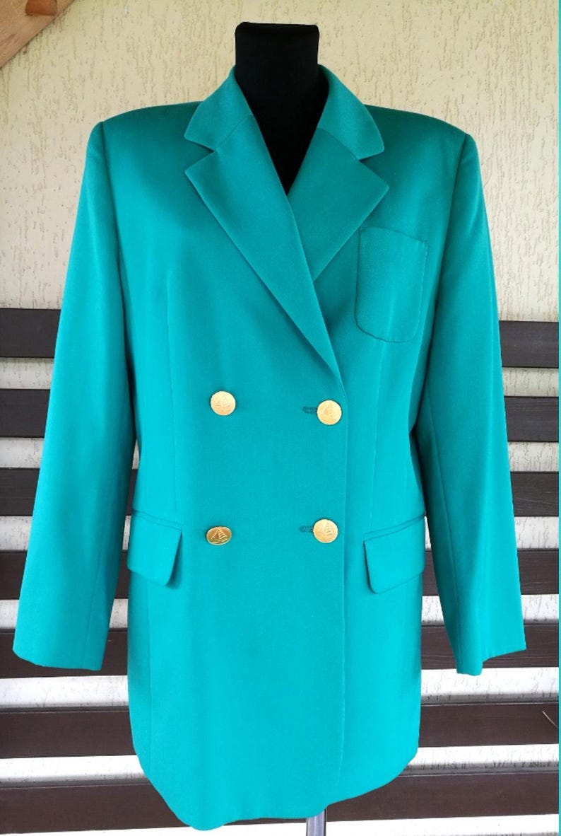 May include: A teal blazer with gold buttons. The blazer has a double breasted closure and a flap pocket on the left side.