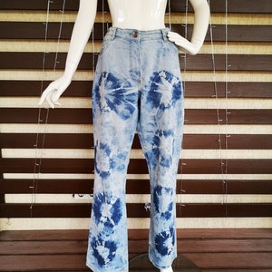 Peut inclure: Un jean en denim bleu avec un motif tie-dye. Le jean a une jambe large et une coupe décontractée.