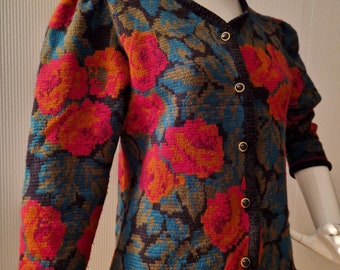 May include: A floral patterned cardigan with a dark blue, green, and orange color scheme. The cardigan has a v-neck and button closure.