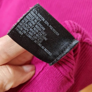May include: A black care label with white text detailing the fabric content and care instructions for a garment. The label reads "67% Rayon 33% Polyester", "RN#93677", "Made in Jordan", "Machine wash cold", "Use only non-chlorine bleach when needed", "Reshape and dry flat", "Iron on lowest setting as needed", and "741868".