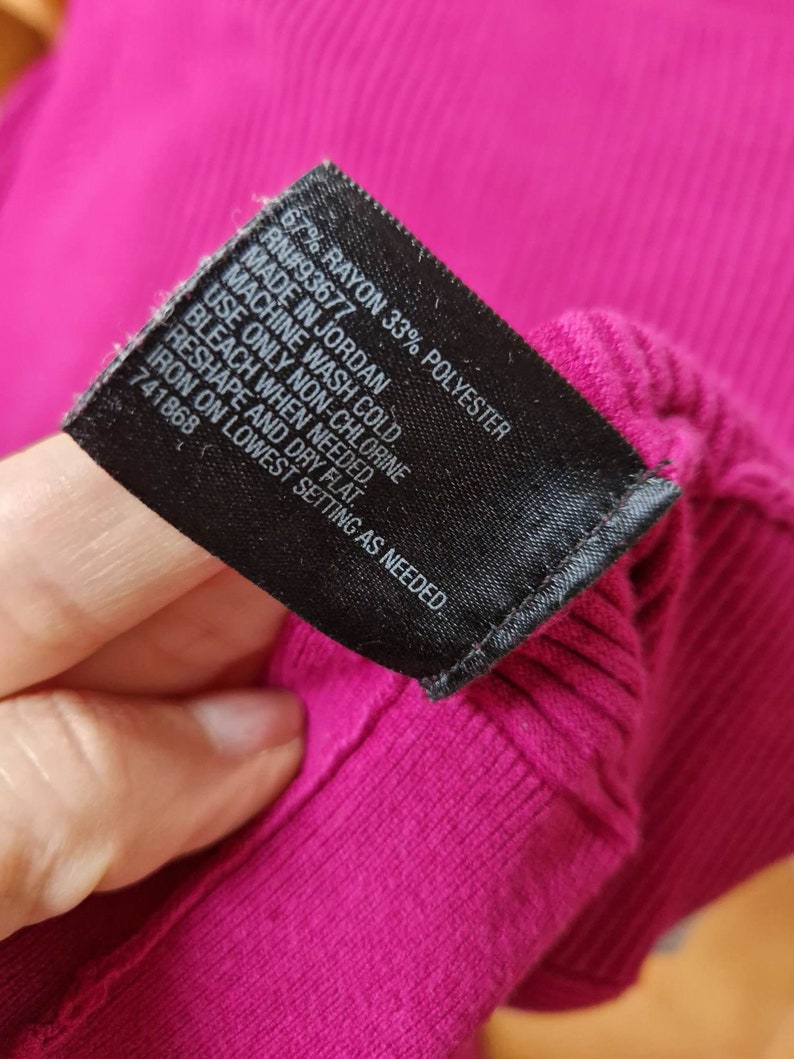 May include: A black care label with white text detailing the fabric content and care instructions for a garment. The label reads "67% Rayon 33% Polyester", "RN#93677", "Made in Jordan", "Machine wash cold", "Use only non-chlorine bleach when needed", "Reshape and dry flat", "Iron on lowest setting as needed", and "741868".