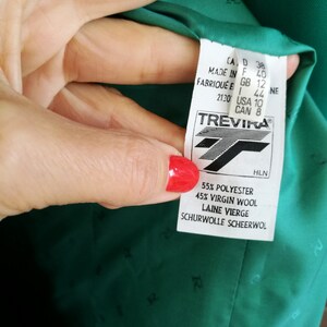 May include: A green blazer with a Trevira label. The label indicates the fabric is 55% polyester and 45% virgin wool. The label also includes sizing information in US, Canadian, UK, European, and Italian sizes.