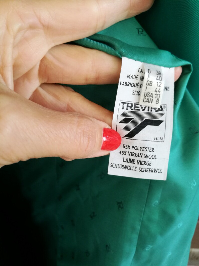 May include: A green blazer with a Trevira label. The label indicates the fabric is 55% polyester and 45% virgin wool. The label also includes sizing information in US, Canadian, UK, European, and Italian sizes.