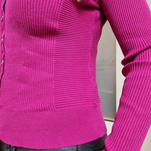 May include: A close-up of a magenta ribbed cardigan with a button-up front and long sleeves. The cardigan is made of a soft, stretchy material and has a fitted silhouette.