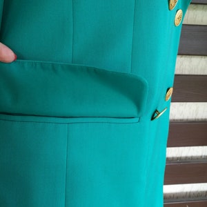 May include: A teal blazer with a single pocket on the left side and gold buttons on the right side.