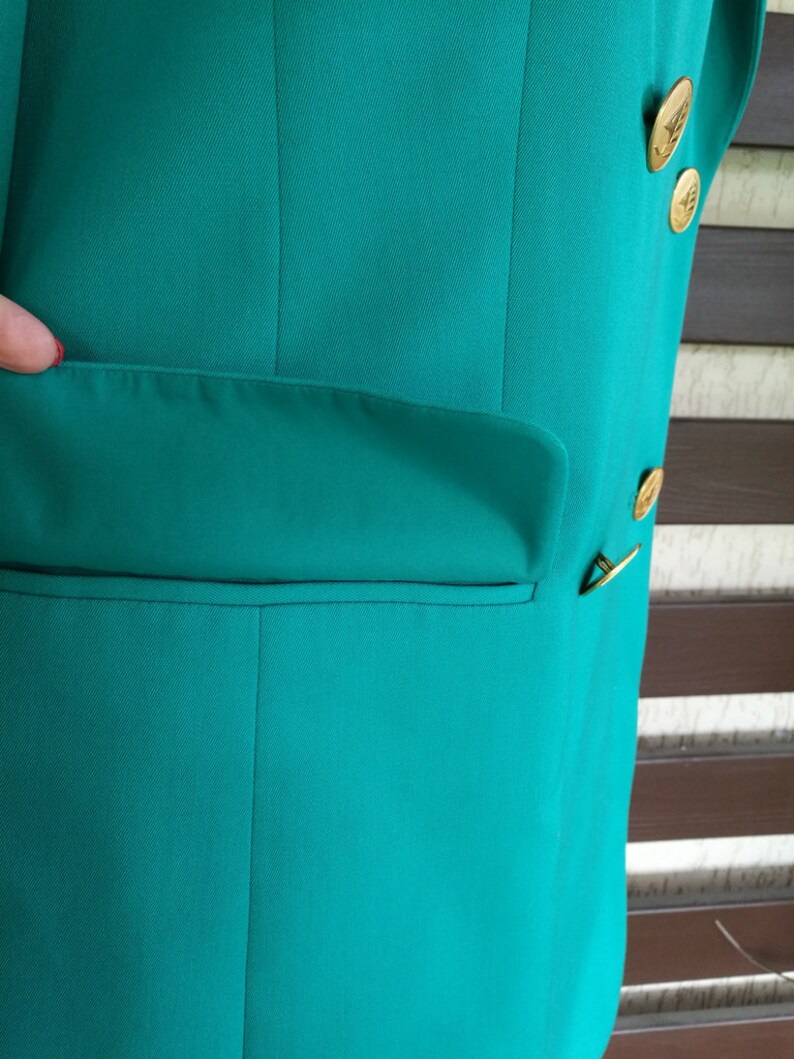 May include: A teal blazer with a single pocket on the left side and gold buttons on the right side.