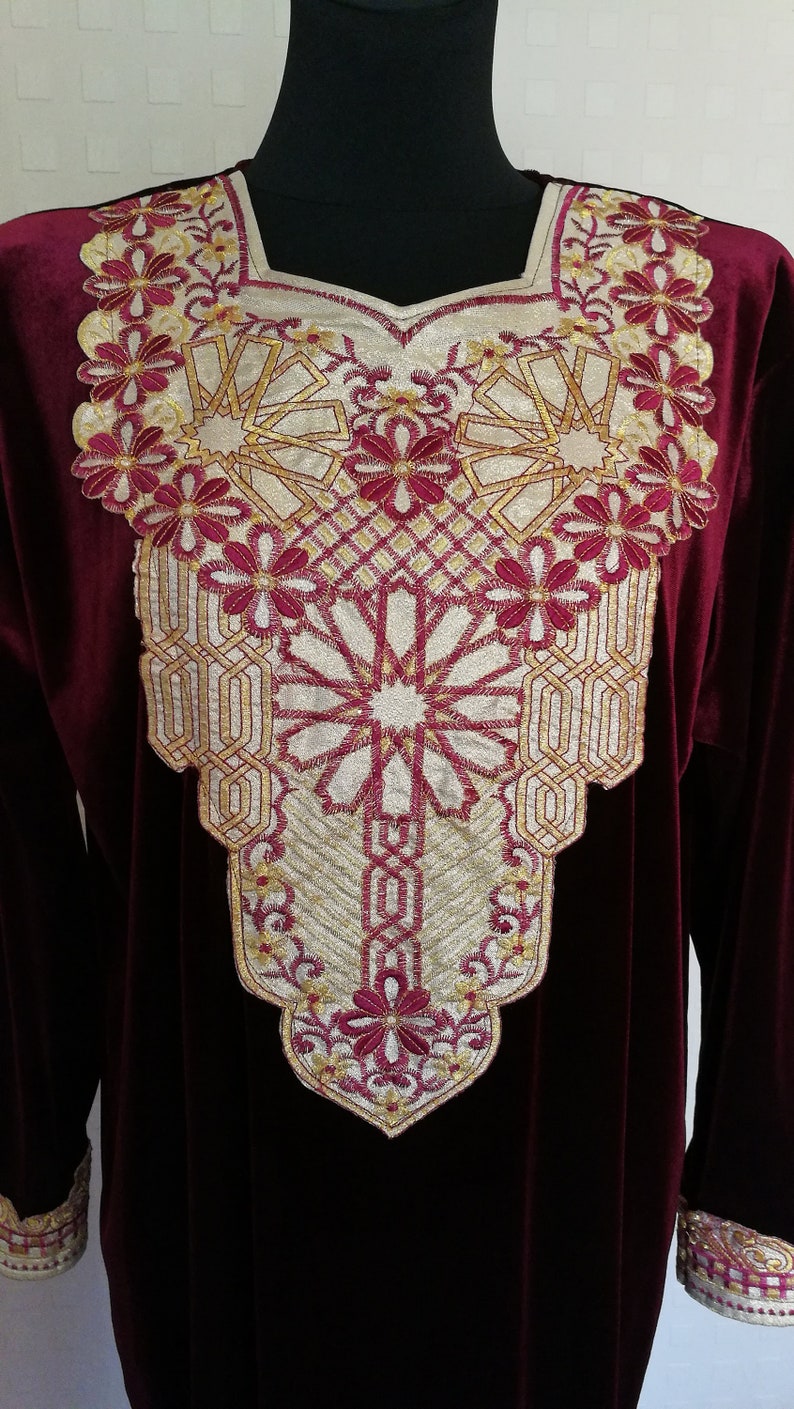 May include: A burgundy velvet dress with gold and burgundy embroidery around the neckline. The embroidery features a geometric pattern with floral accents.