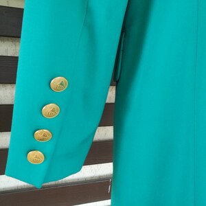 May include: Teal blazer with gold buttons featuring a geometric design. The buttons are on the sleeve of the blazer.