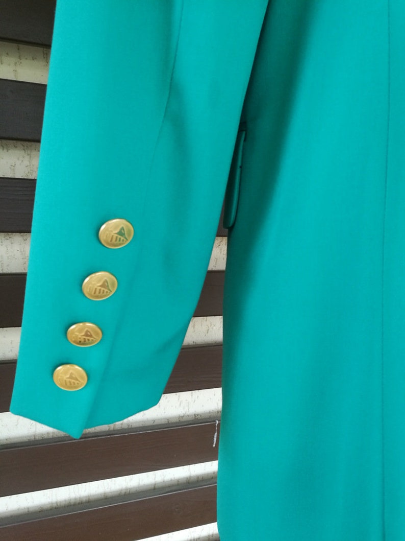 May include: Teal blazer with gold buttons featuring a geometric design. The buttons are on the sleeve of the blazer.