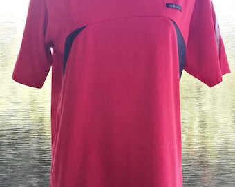 May include: A red short-sleeved t-shirt with black and white stripes on the shoulders and sleeves. The shirt has a black panel on the side and a black "adidas" logo on the front.