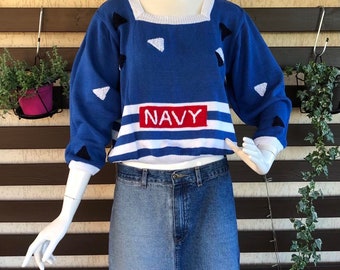 May include: A blue and white striped sweater with a red "NAVY" patch and black triangle designs. The sweater is worn over a denim skirt.