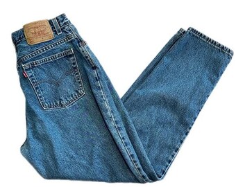 May include: Blue denim jeans with a classic five-pocket design. The jeans feature a faded wash and a straight leg cut. A brown leather patch is visible on the back waistband. The jeans are folded and laid flat.