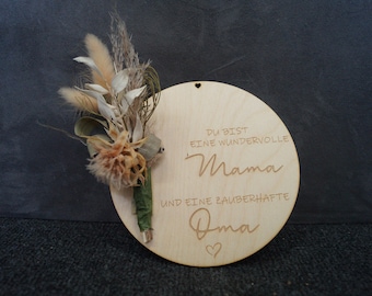 Könnte beinhalten: Eine kreisförmige Holzplatte in hellem Farbton mit einem kleinen Strauß aus getrockneten Blumen und Gräsern auf der linken Seite. Der Text lautet: DU BIST EINE WUNDERVOLLE Mama UND EINE ZAUBERHAFTE Oma, mit einem kleinen Herzsymbol oben und unten.