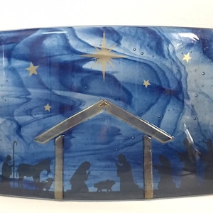 Peut inclure: Une œuvre d'art en verre bleu représentant la scène de la nativité avec une crèche en argent et or, une étoile et des silhouettes de personnes et d'animaux.