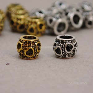May include: Two heart-shaped bead spacers, one gold and one silver, with a detailed design. The beads are round and have a hole in the center for threading.