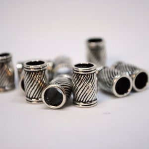May include: Silver metal beads with a twisted design. The beads have a hole in the center and are approximately 1/2 inch in diameter.
