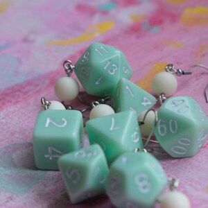 May include: A set of six mint green dice earrings with white numbers. The dice are attached to silver earring hooks with white beads.