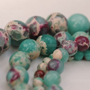 May include: A strand of green and pink marbled gemstone beads. The beads are round and have a speckled appearance.