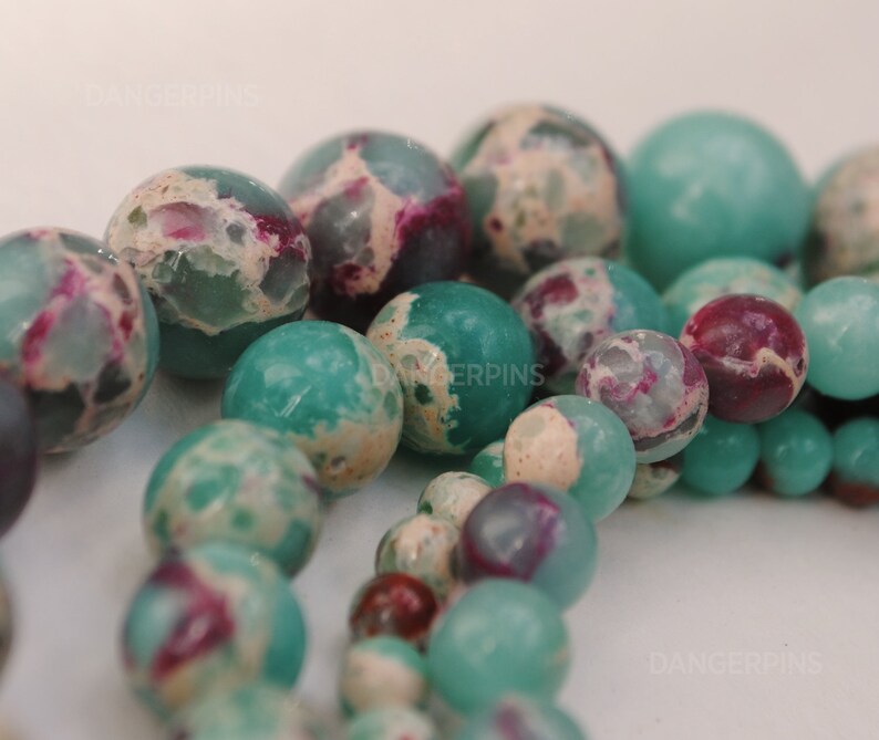 May include: A strand of green and pink marbled gemstone beads. The beads are round and have a speckled appearance.