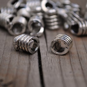 May include: Silver metal beads with a ridged design. The beads have a hole in the center and are designed to be used as hair ties or jewelry.