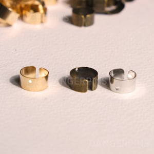 May include: Three metal rings in gold, bronze, and silver. The rings are open on one side and have a small hole on the other side.