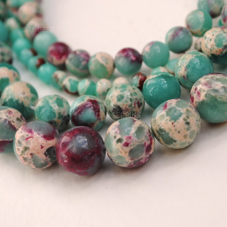 May include: A strand of green and white speckled beads with hints of pink and purple. The beads are round and have a smooth, polished finish.
